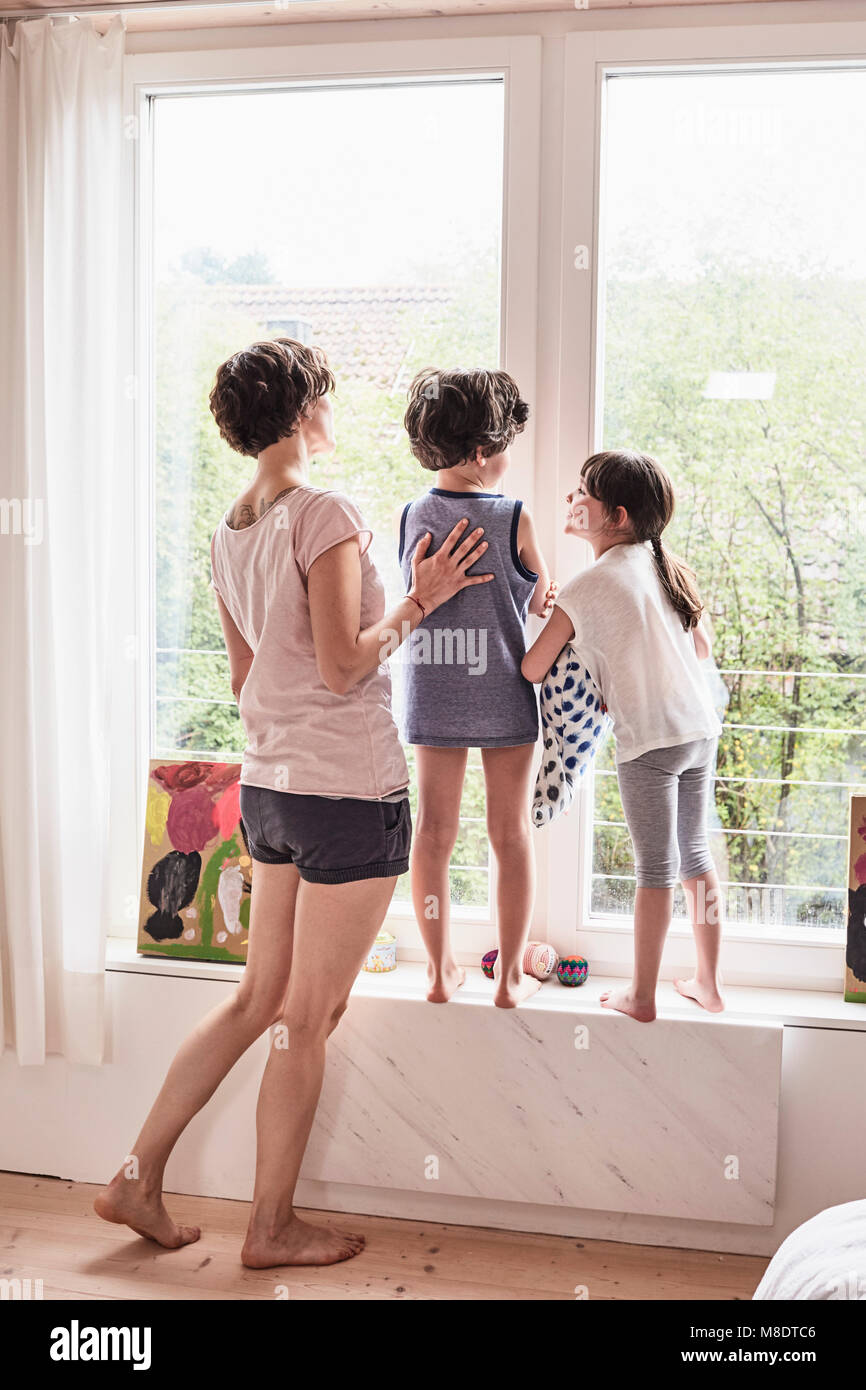Mother, son and daughter at home, looking out of window, rear view Stock Photo