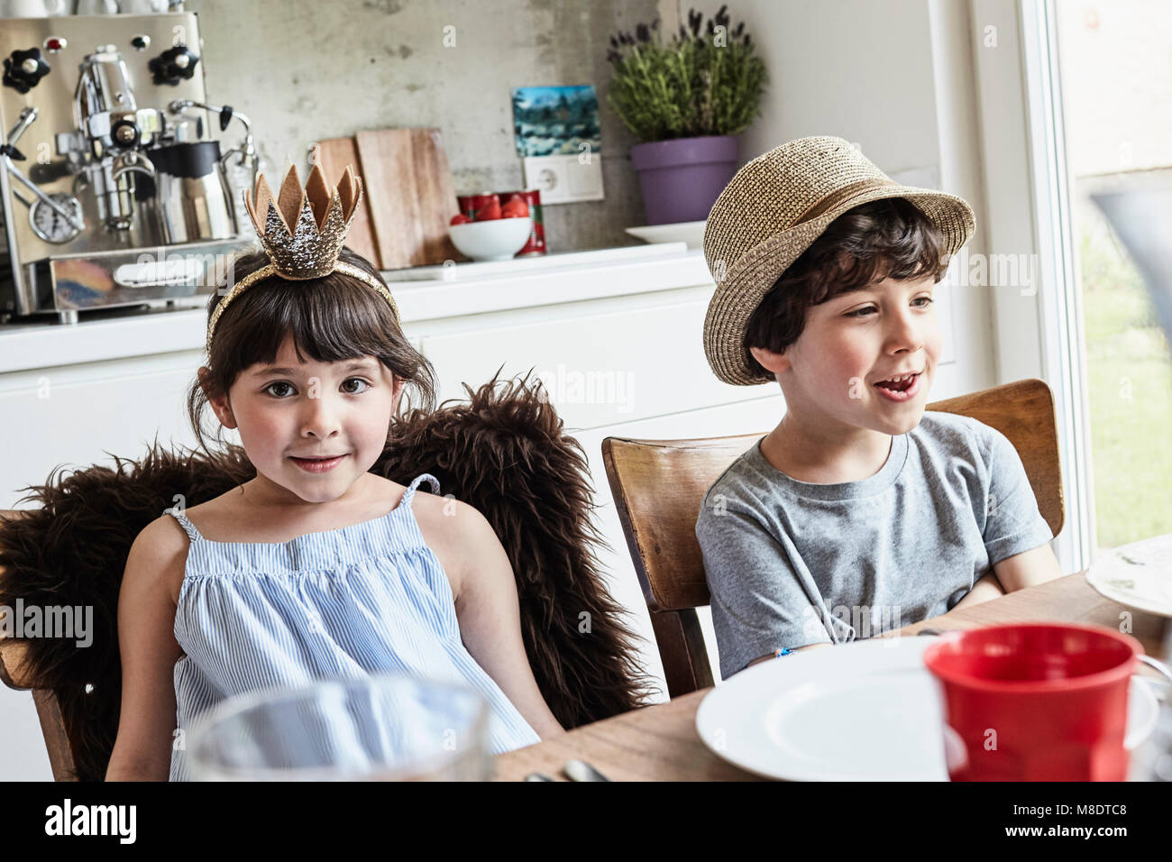 Brother and sister sitting at dinner table, smiling Stock Photo