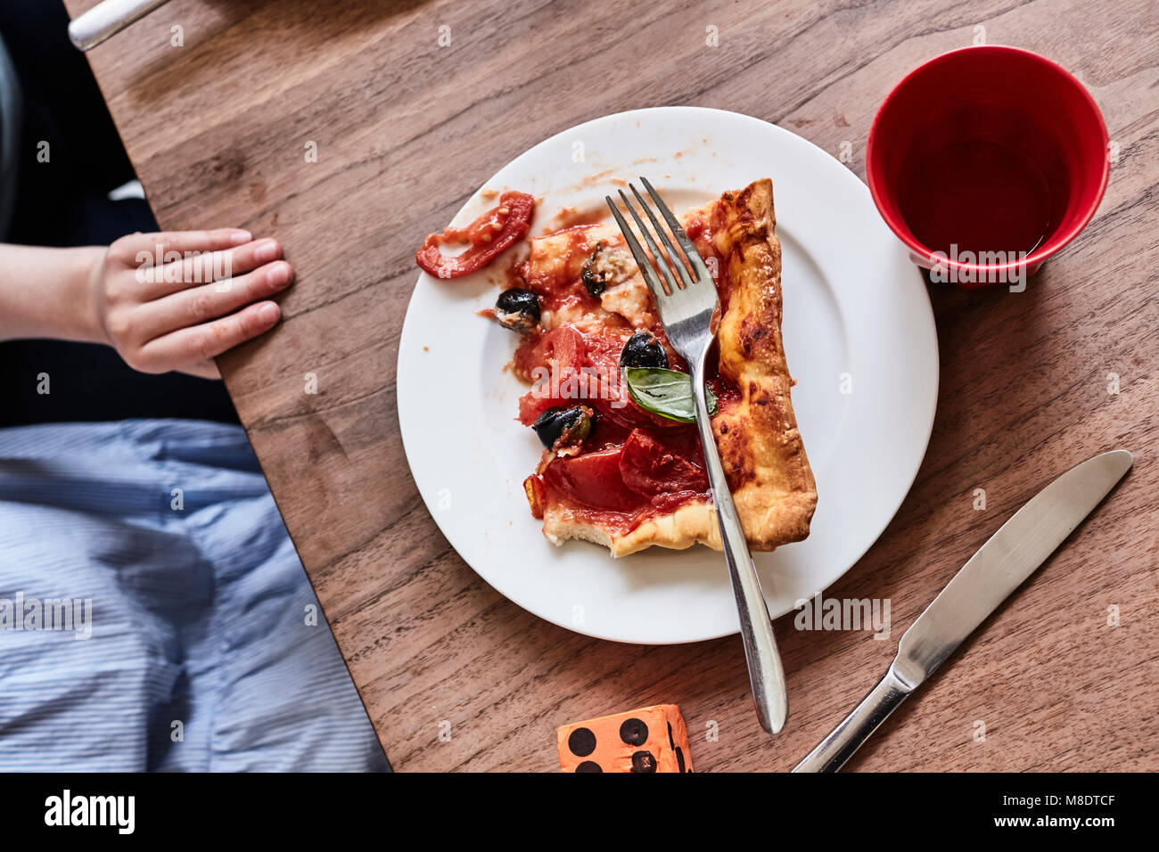 Slice of pizza on white plate, child's hand on table, mid section, elevated view Stock Photo