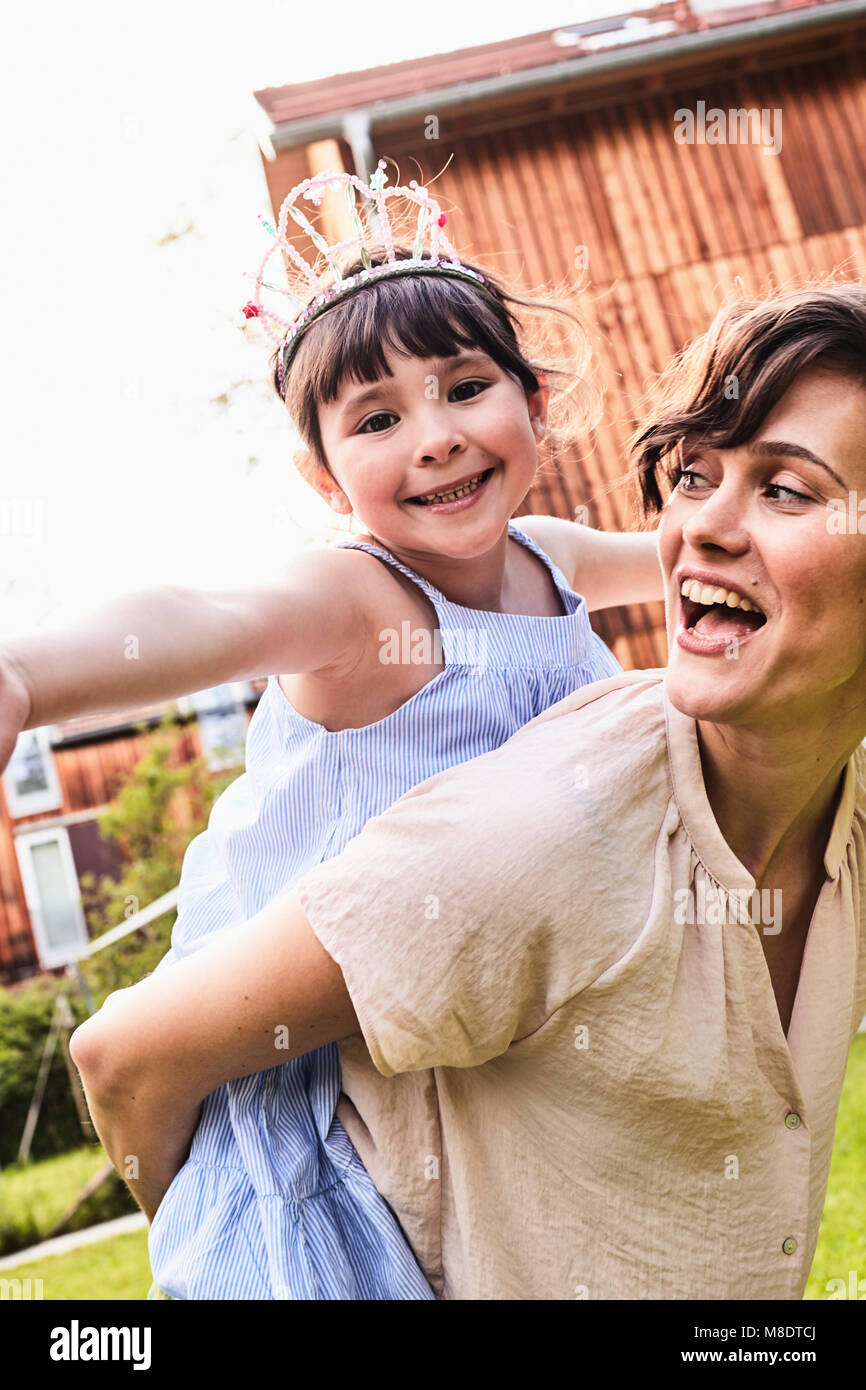 Portrait of mother carrying daughter on back, smiling Stock Photo