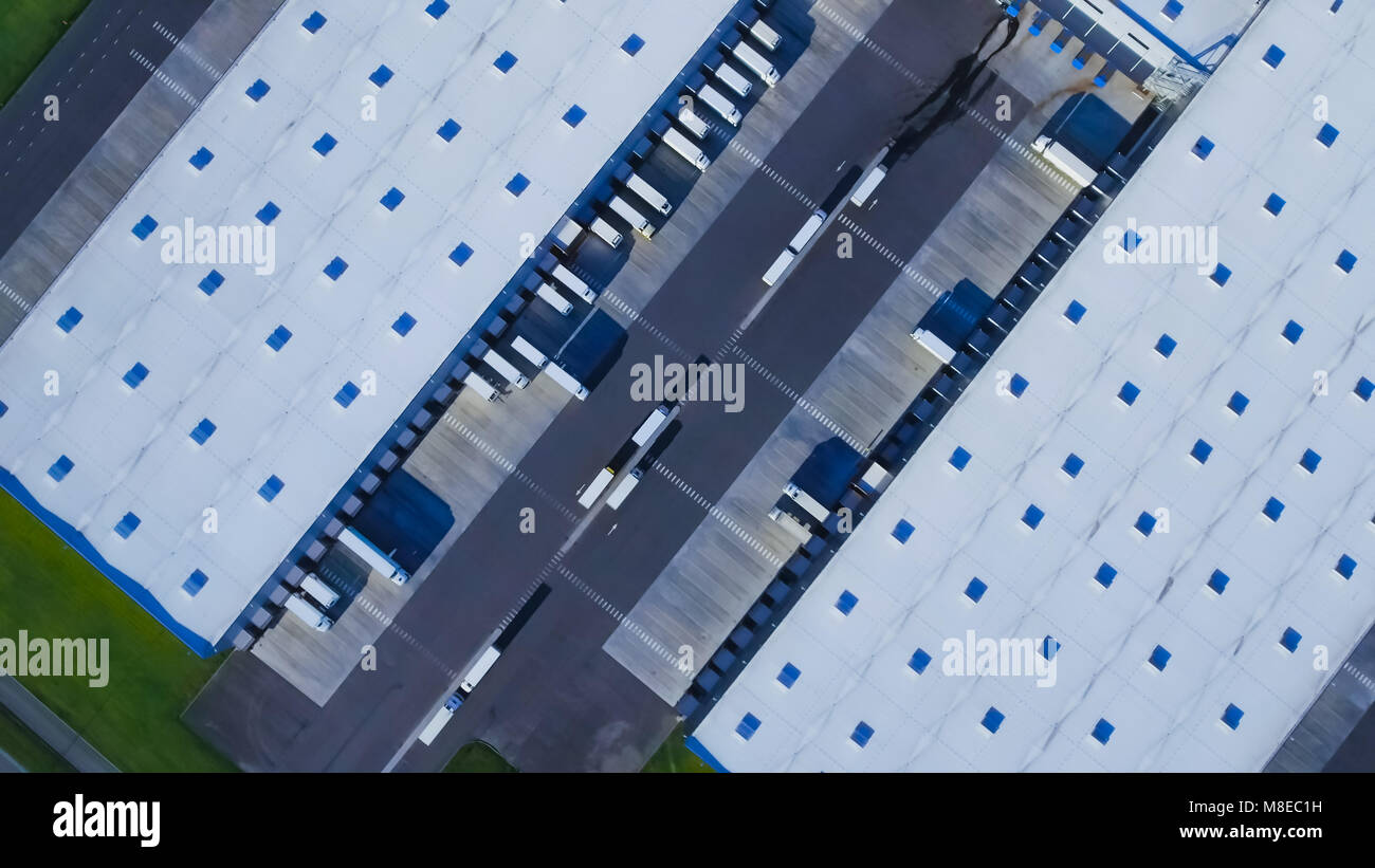 Aerial Top View of Industrial Warehouse/ Storage Building/ Loading Area with Solar Panels on the Roof and Many Trucks Loading/ Unloading Merchandise. Stock Photo