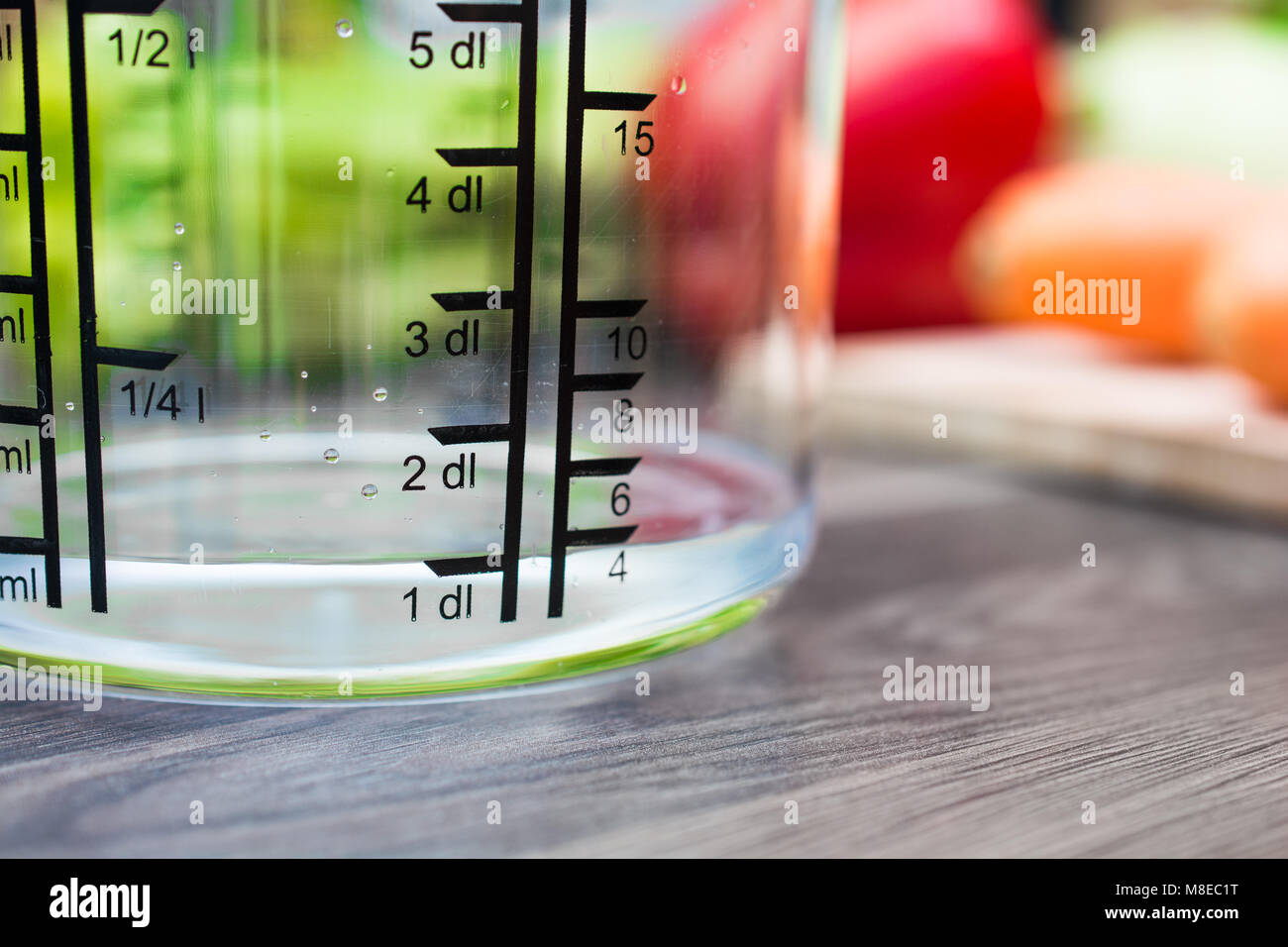 100ml / 1dl Of Water In A Measuring Cup On A Kitchen Counter With Vegetables Stock Photo