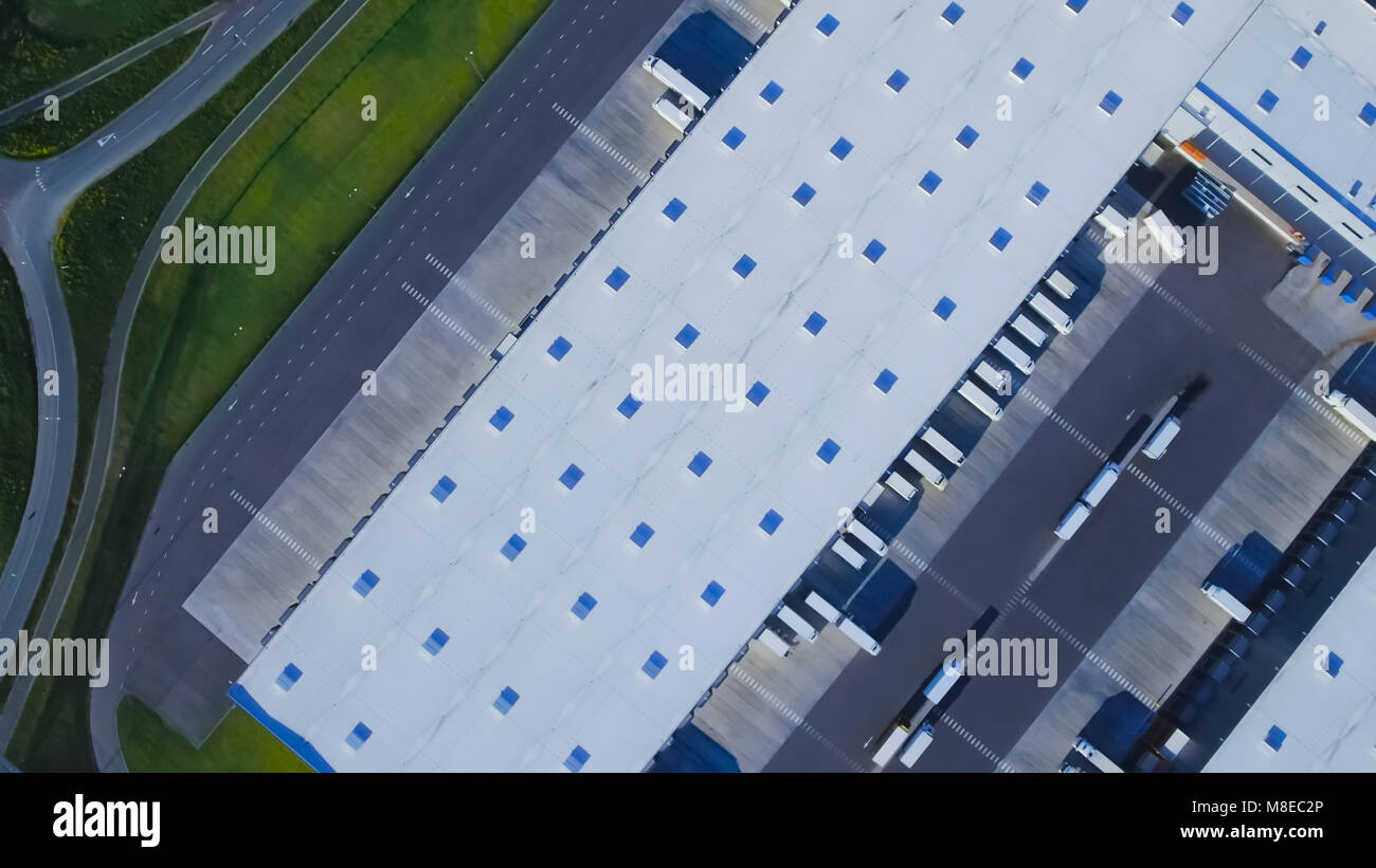 Aerial Top View of Industrial Warehouse/ Storage Building/ Loading Area with Solar Panels on the Roof and Many Trucks Loading/ Unloading Merchandise. Stock Photo
