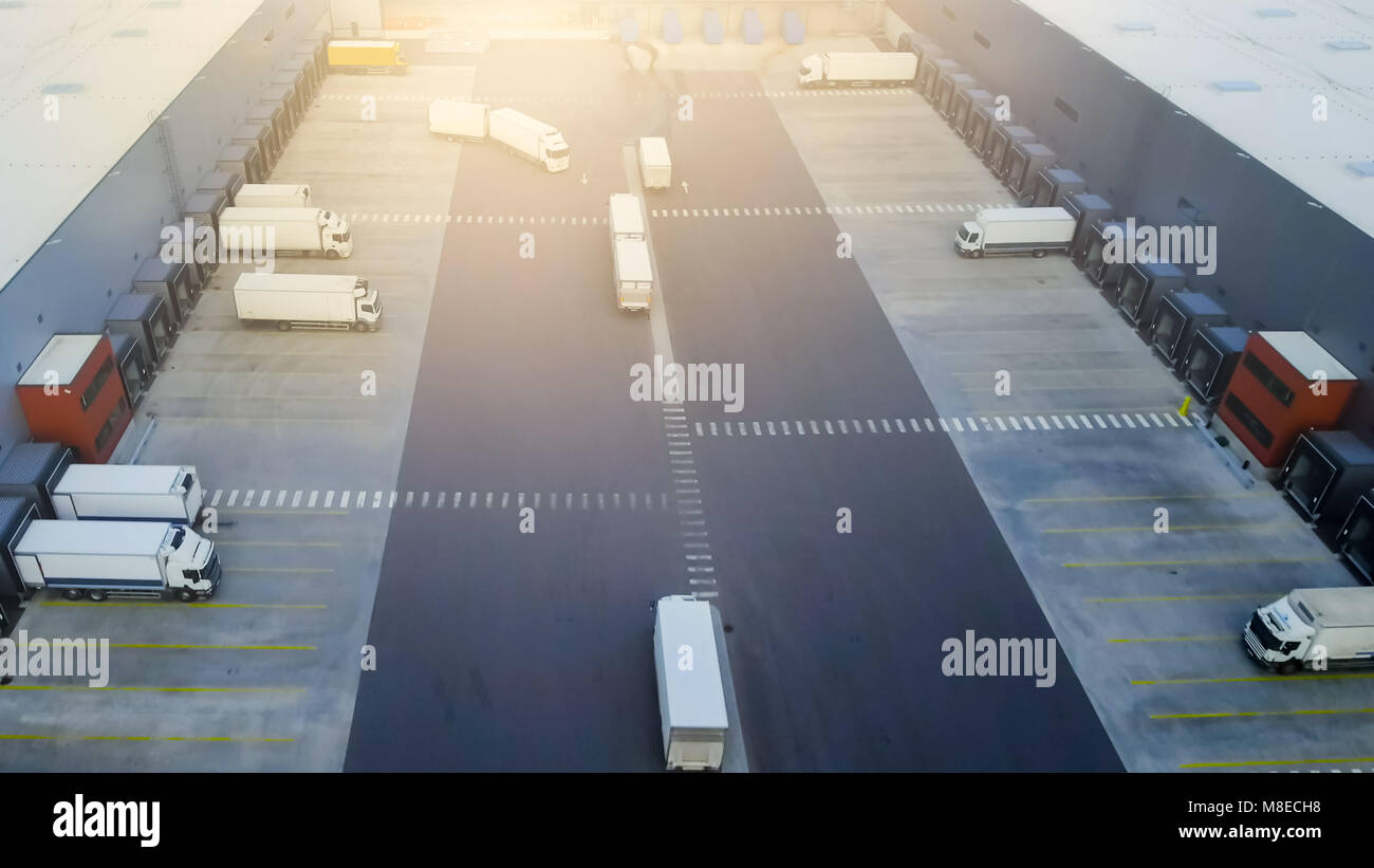 Aerial Shot of Truck with Attached Semi Trailer Leaving Industrial Warehouse/ Storage Building/ Loading Area where Many Trucks Are Loading/ Unloading  Stock Photo