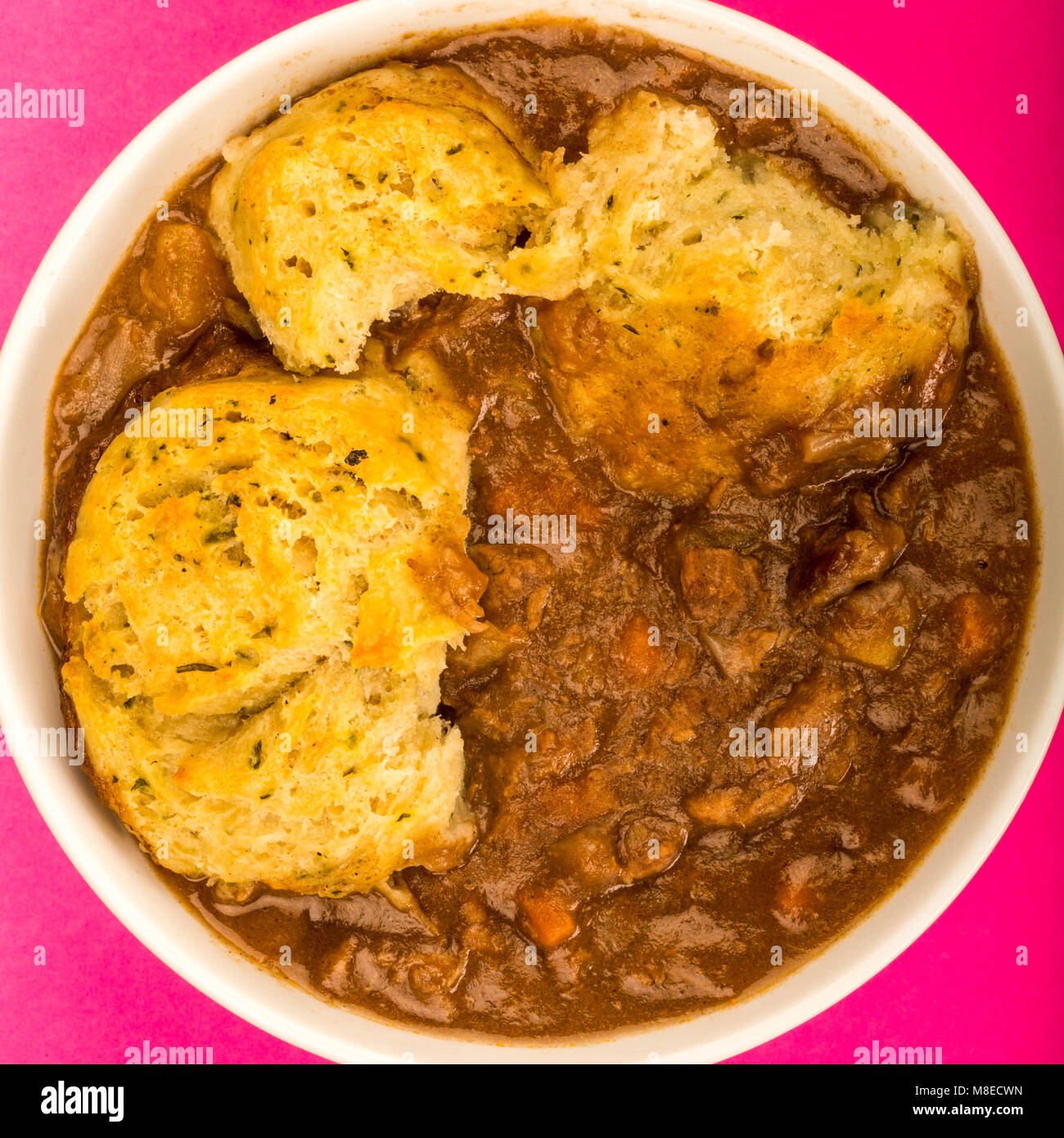 Traditional British Beef Casserole With Dumplings Against A Pink Background Stock Photo