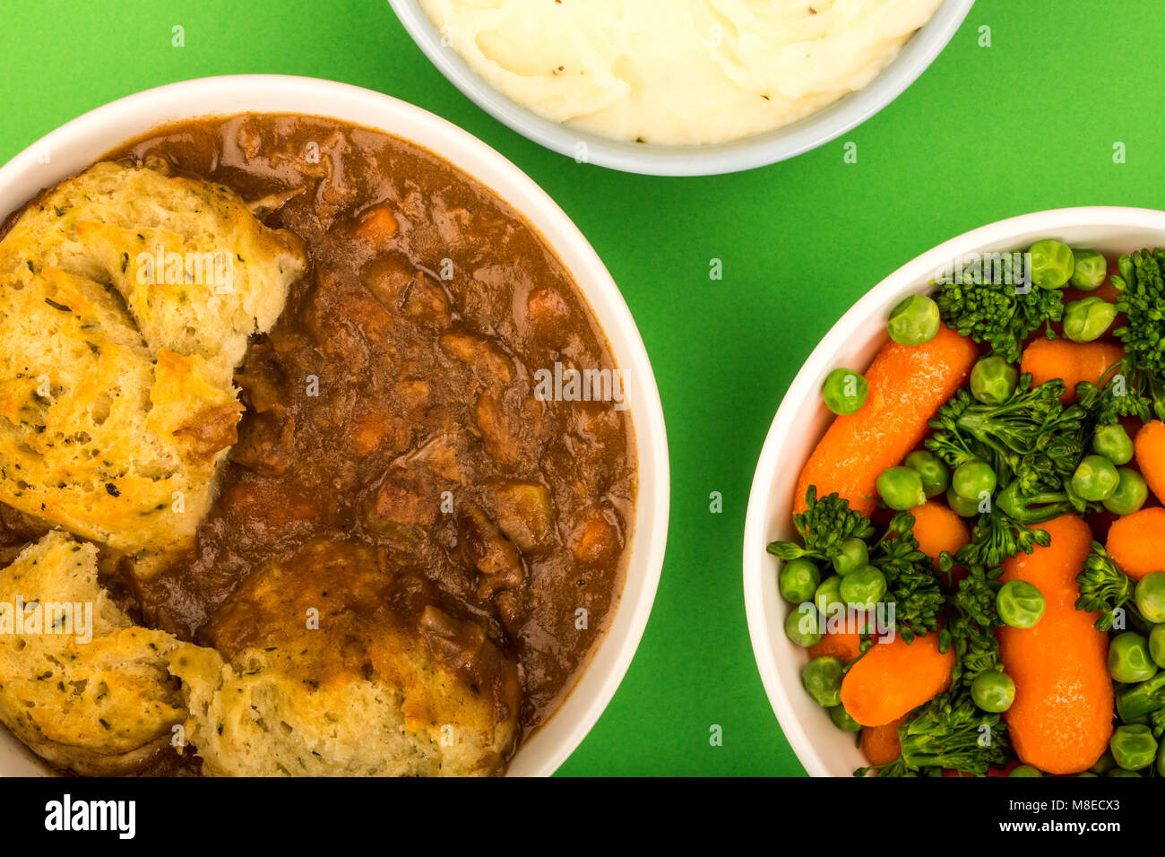 Traditional British Beef Casserole With Dumplings Against A Green Background And A Bowl Of Mashed Potatoes And Mixed Vegetables Stock Photo