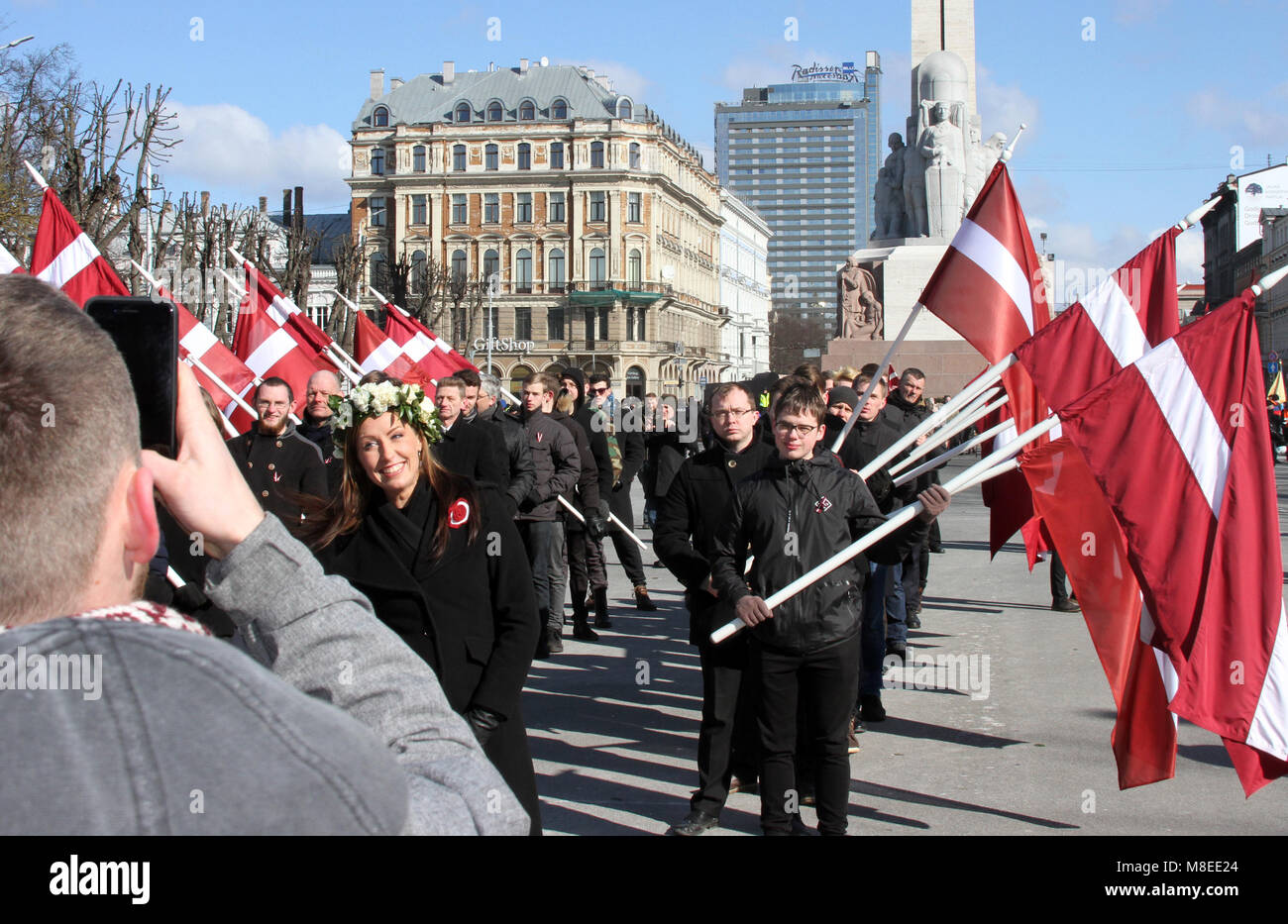 16 March 2018, Latvia, Riga: A young man (L) photographs adolescents holding Latvian flags during a commemoration march for Latvian Waffen-SS veterans in Riga. Latvian veterans of a unit of the Waffen-SS have commemorated their fallen comrades with the controversial march. On Friday about 1500 participants in the war and sympathisers marched through the capital of the Baltic EU and NATO country with massive police protection. Photo: Alexander Welscher/dpa Stock Photo