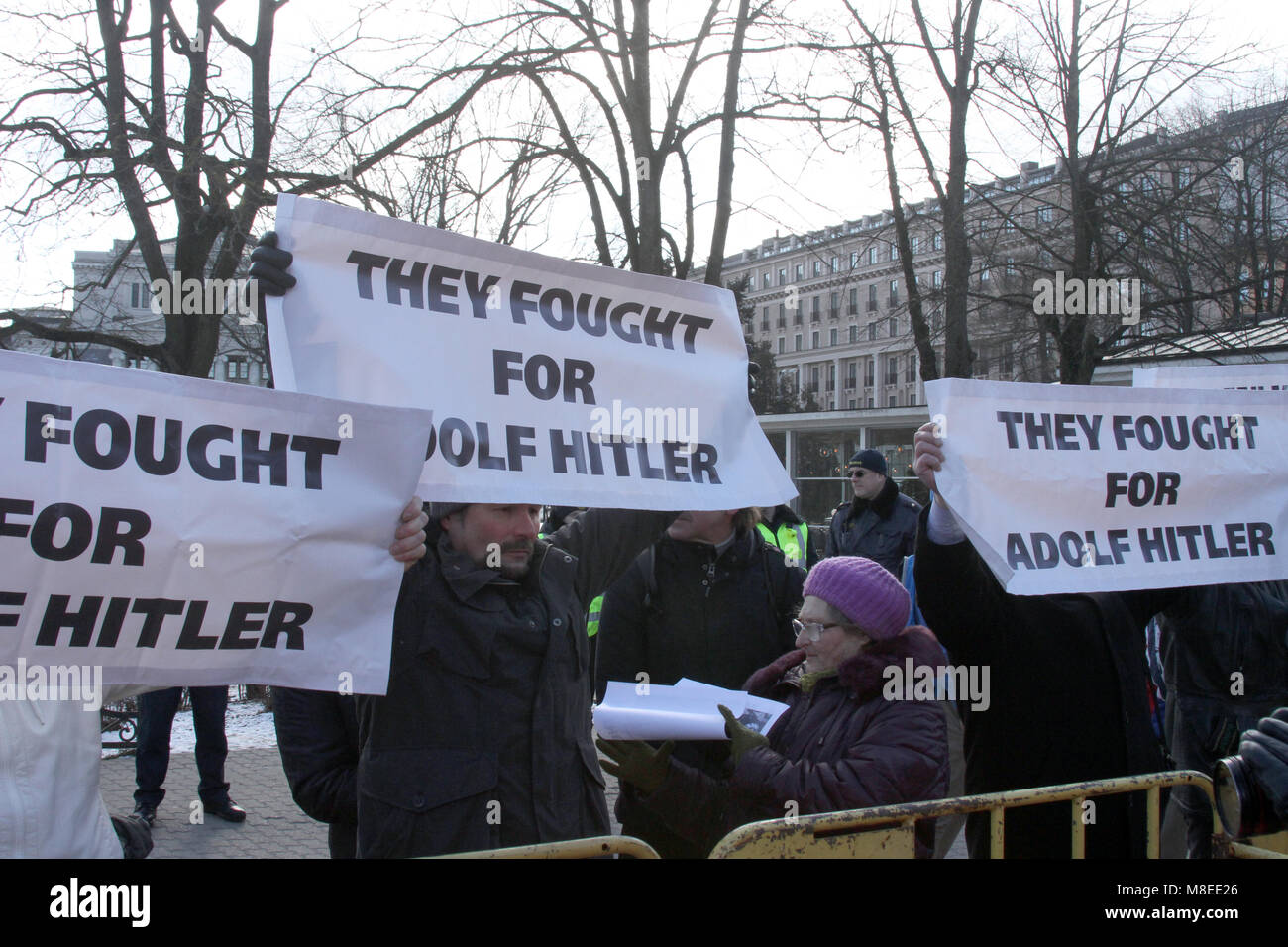 16 March 2018, Latvia, Riga: Counter-demonstrators holding up a posters reading 'they fought for Adolf Hitler' at a barrier by a freedom monument during a commemoration march for Latvian Waffen-SS veterans in Riga. Latvian veterans of a unit of the Waffen-SS have commemorated their fallen comrades with the controversial march. On Friday about 1500 participants in the war and sympathisers marched through the capital of the Baltic EU and NATO country with massive police protection. Photo: Alexander Welscher/dpa Stock Photo