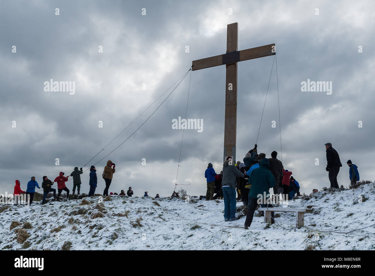 Otley Chevin, UK, 17th March 2018. On a cold, snowy morning, volunteers from the local churches, using ropes, raise the enormous, heavy, wooden, Easter Cross on The Chevin, a high ridge overlooking the town of Otley, West Yorkshire, England, UK. A Christian symbol of faith & hope. Credit: Ian Lamond/Alamy Live News Stock Photo