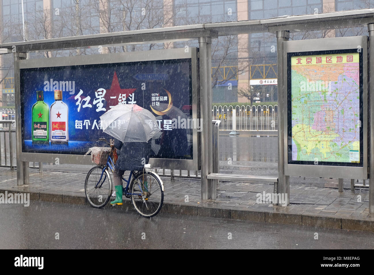 Beijing, China, March 17, 2018. Rare Snowy Day in Chaoyang District, Beijing, China. A person on a bicycle holding an umbrella beside an advertising board on a snowy day. Credit: Steven Liveoak/Alamy Live News Stock Photo
