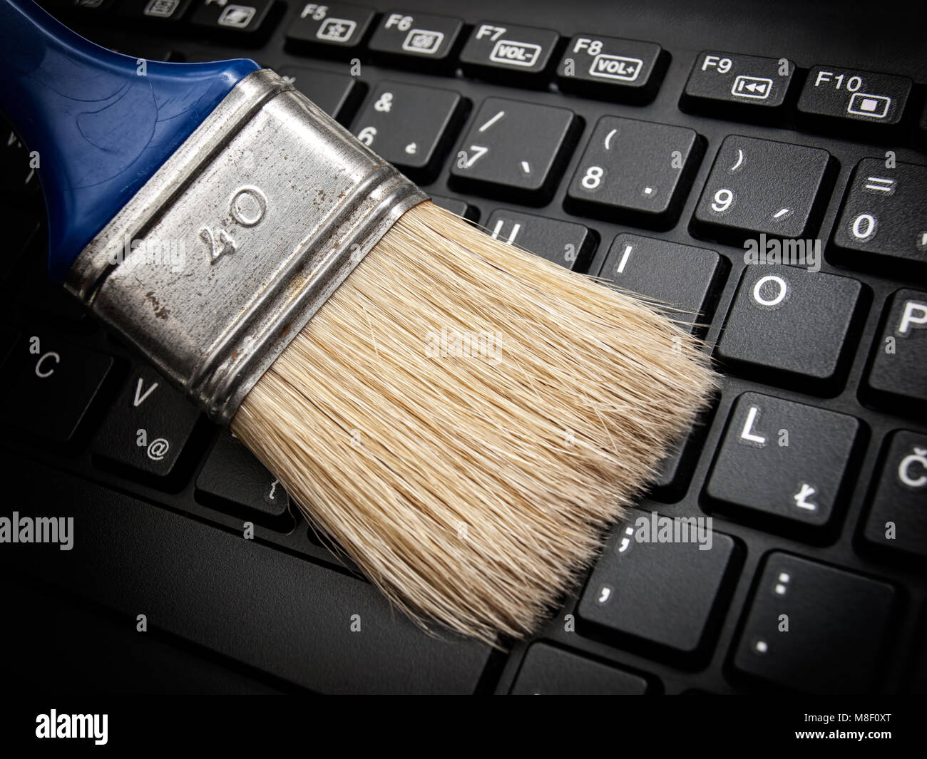 The brush cleans the computer keyboard as a concept of maintaining digital data. Stock Photo