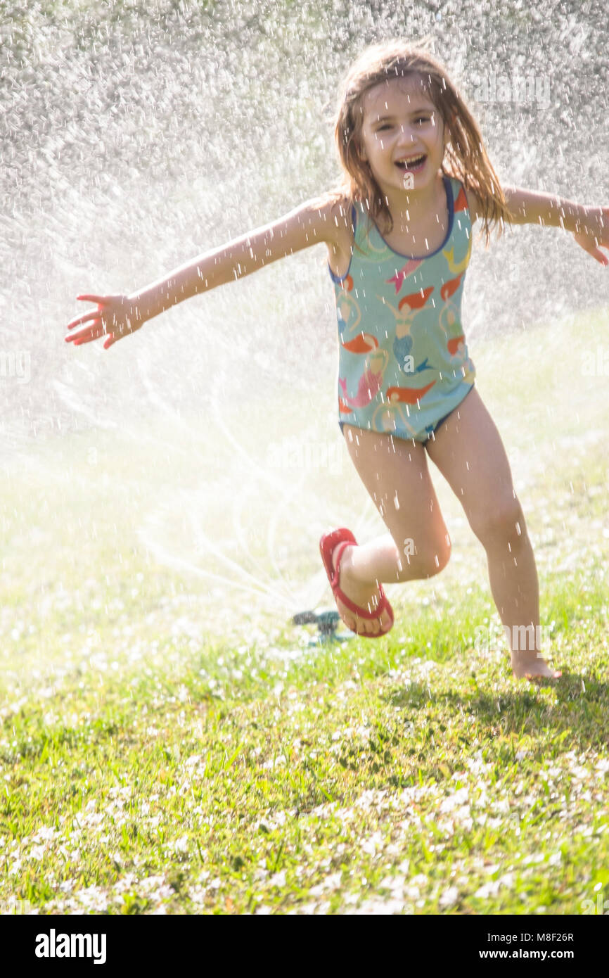 Girl (4-5) splashing in sprinkler water on lawn Stock Photo