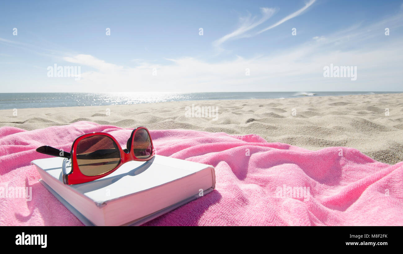 Book and sunglasses on pink towel on sandy beach Stock Photo - Alamy