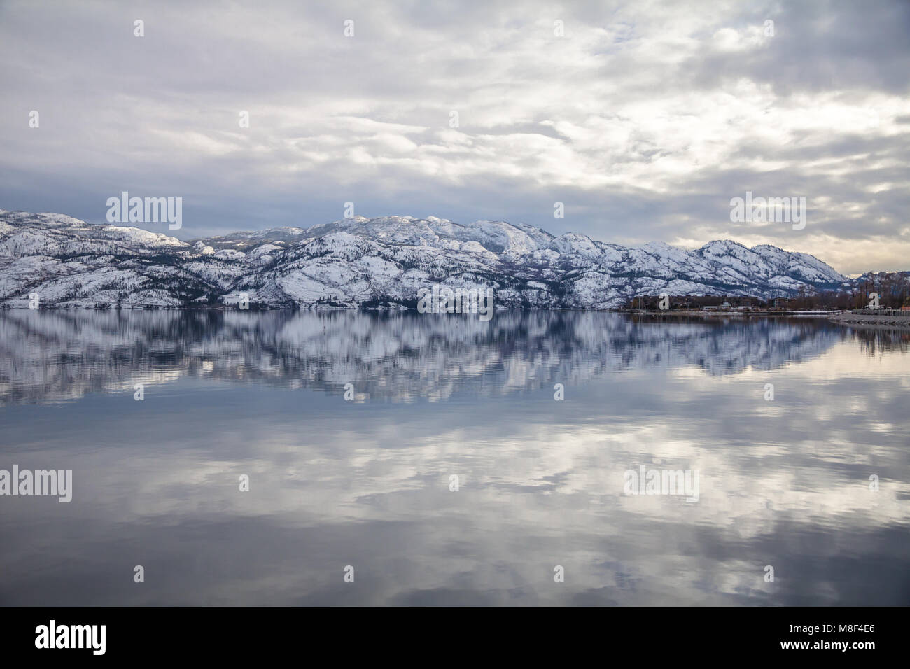 Snow-covered mountains reflect symetrically in Okanagan Lake, West Kelowna Stock Photo