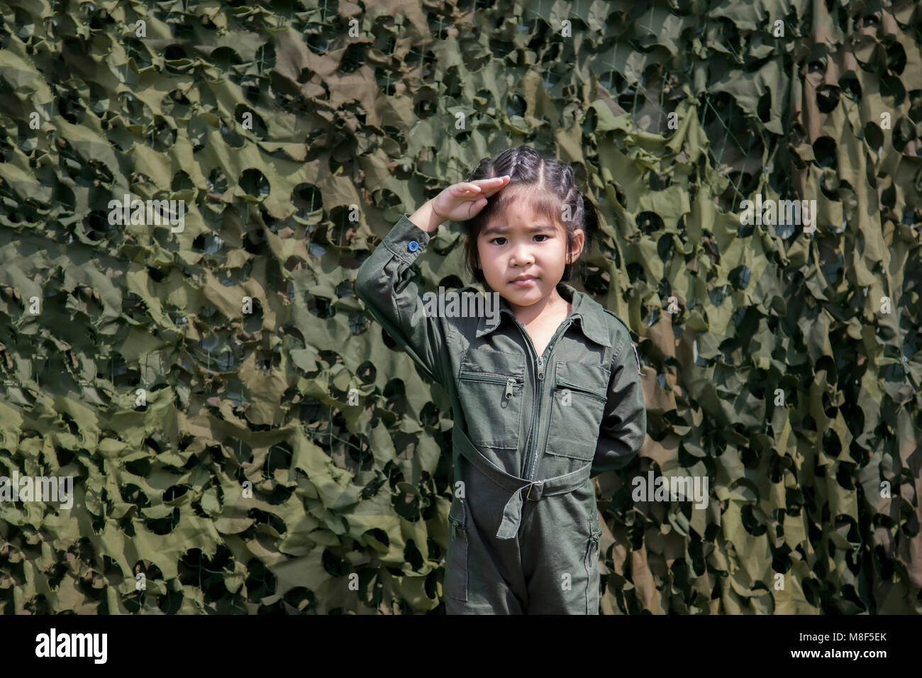 asian girl respect soldier action with green soldier or pilot uniform on green texture net bunker background Stock Photo