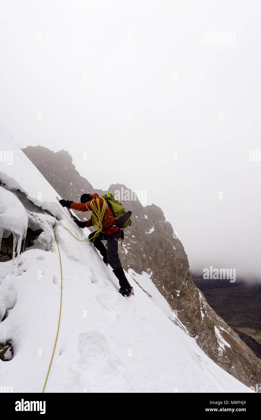 male mountain guide climbing a steep glacier in the Andes in Peru during a mountaineering expedition in bad weather Stock Photo