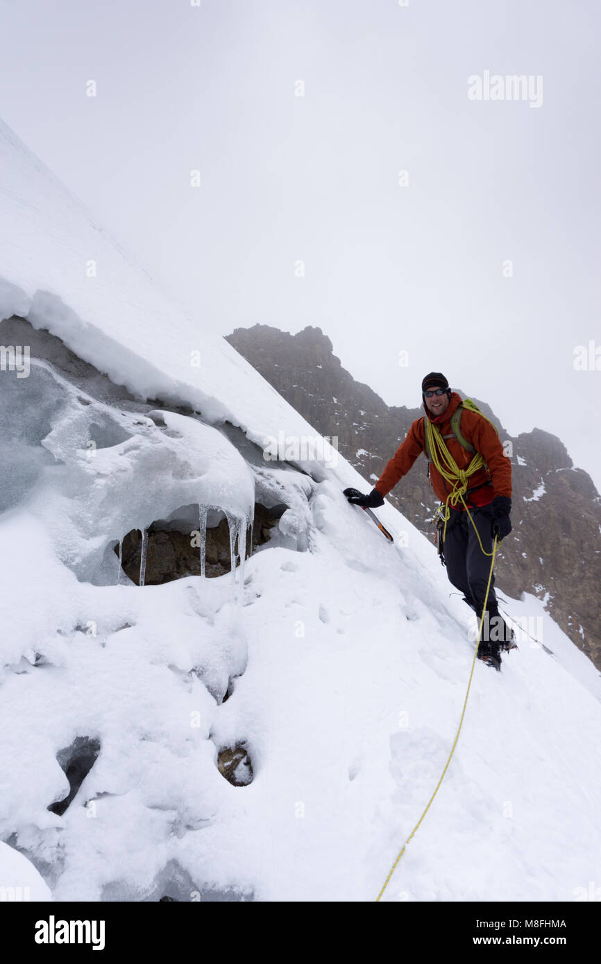 male mountain guide climbing a steep glacier in the Andes in Peru during a mountaineering expedition in bad weather Stock Photo