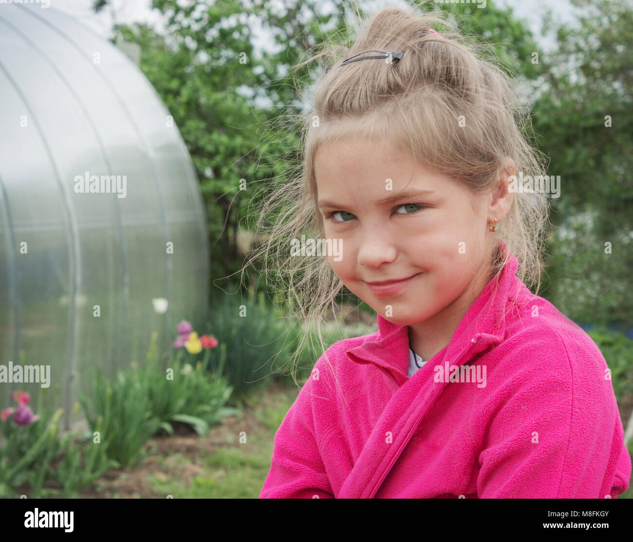 Girl with a sly smile on her face and in a red jacket in the garden