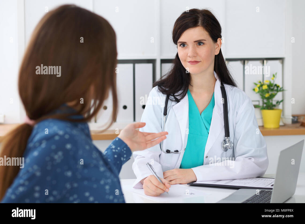 Beautiful female doctor and patient having a talk while sitting at the ...