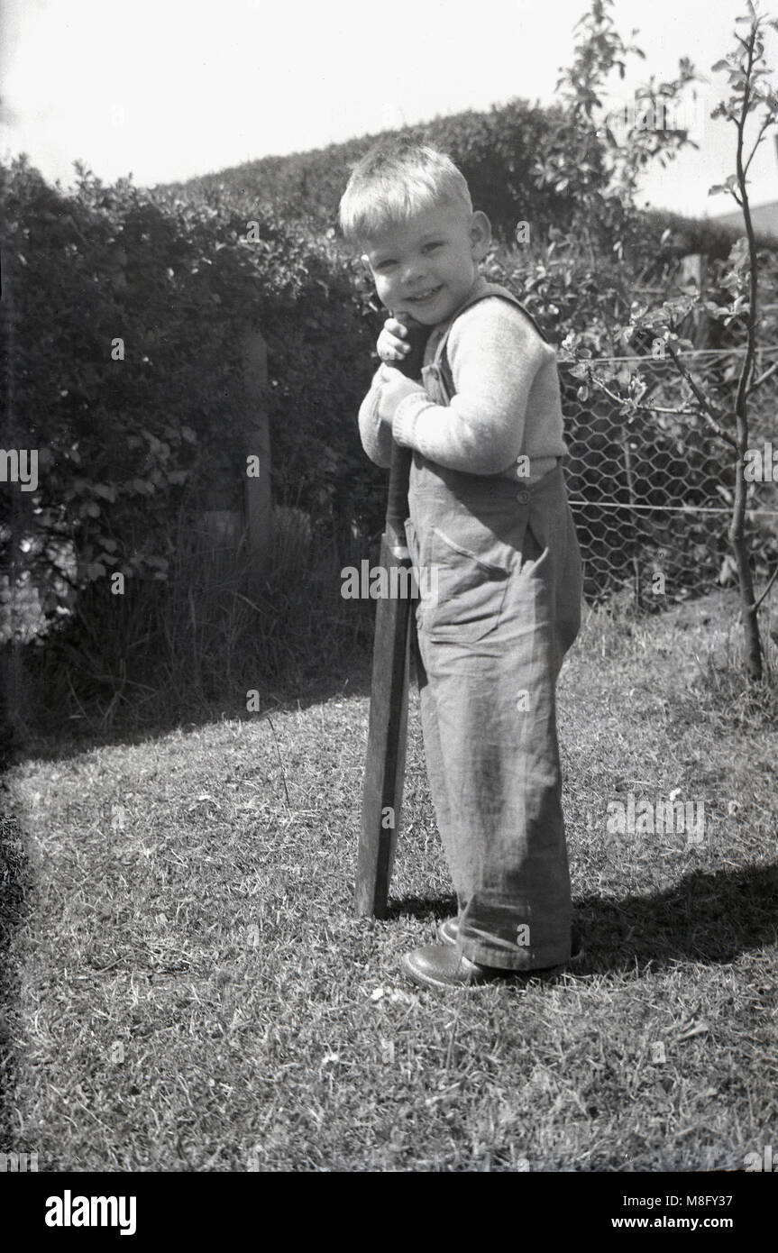1950, historical, summertime and outside in a back garden, a young boy holding onto an old cricket bat, England, UK. Stock Photo