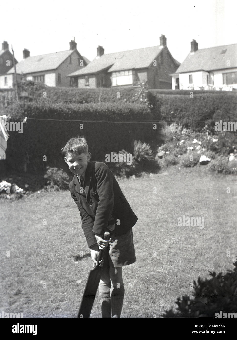 1950, historical, summertime and outside in a suburban back garden, a schoolboy in jacket and shorts holding an old cricket bat, England, UK. Stock Photo
