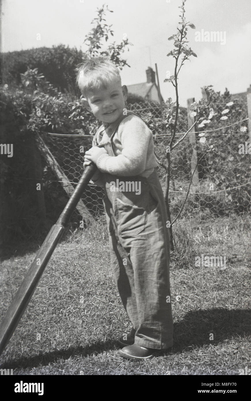 1950, historical, summertime and outside in a back garden, a young boy holding onto an old cricket bat, England, UK. Stock Photo