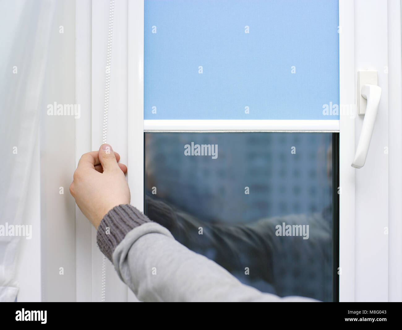 Male hand lifting or closing blinds on a window, indoor closeup Stock Photo