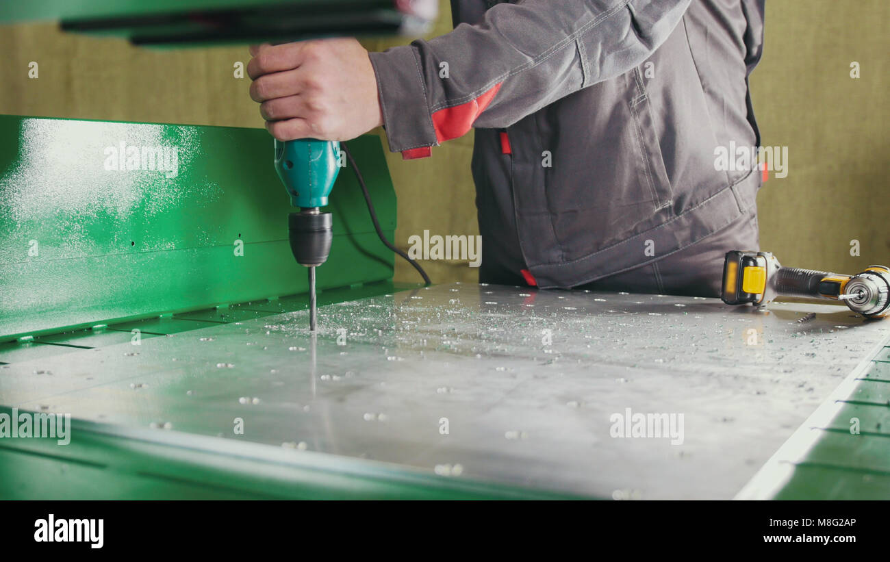 Close up of drill running by worker's hands and drilling metal plate