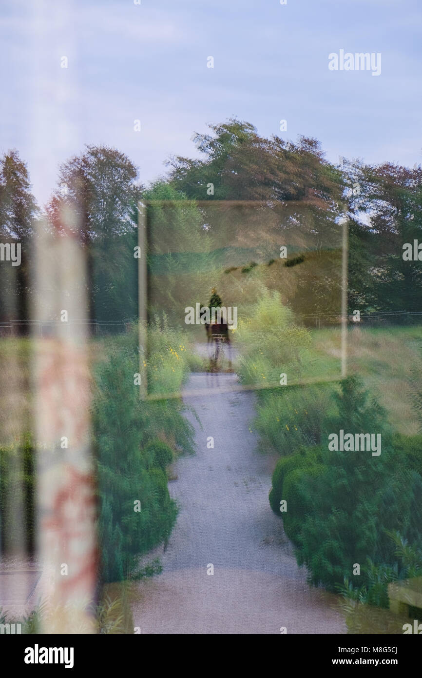 Optical Illusion: A man seems to be riding his horse in a path in the green, however in reality a painting is reflected in the window of a room pointing into the green. Stock Photo