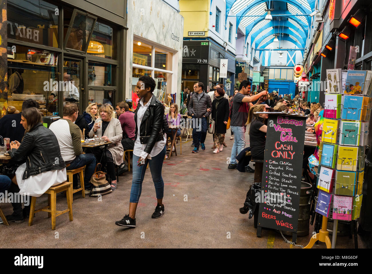 People shopping in the indoor Brixton Village Market, a multicultural community market with independent shops and ethnic restaurants in South London. Stock Photo
