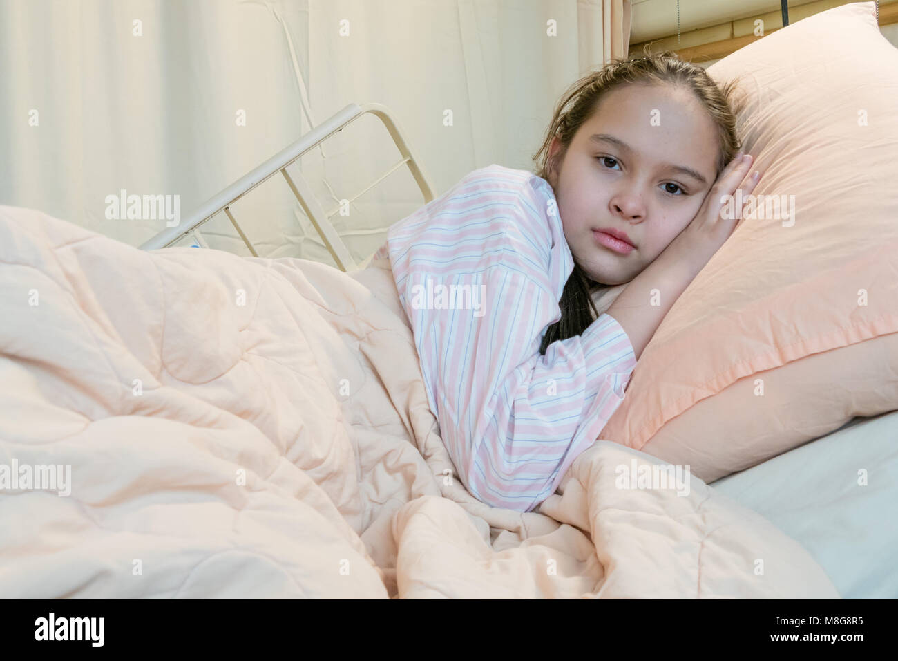 Mixed race tween girl in hospital bed, looking at camera Stock Photo