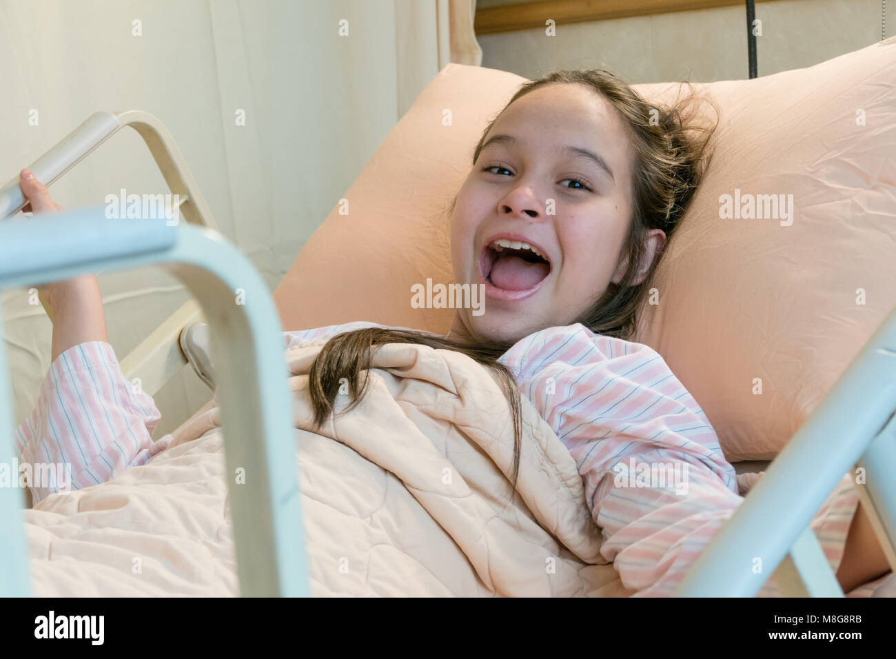Laughing mixed race Asian American tween girl in hospital bed Stock