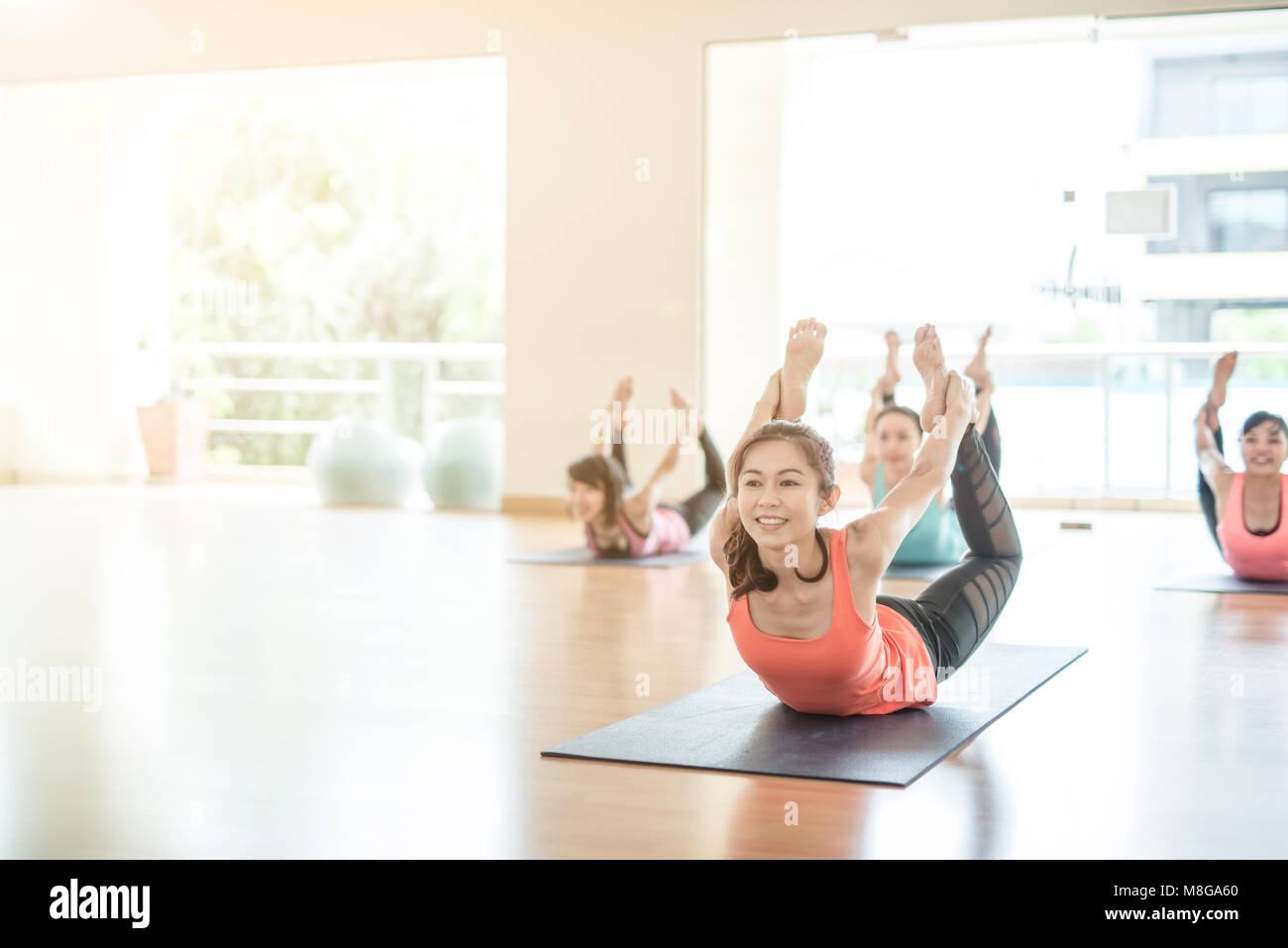 group of smiling aisan woman practicing yoga, stretching in Scorpion exercise, variation of vrischikasana pose, working out, wearing sportswear, pants Stock Photo