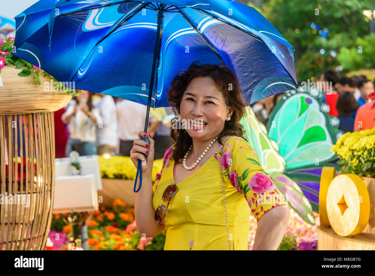 A Vietnamese woman wearing a yellow dress and holding a blue parasol, Ho Chi Minh City, Saigon, Vietnam Stock Photo