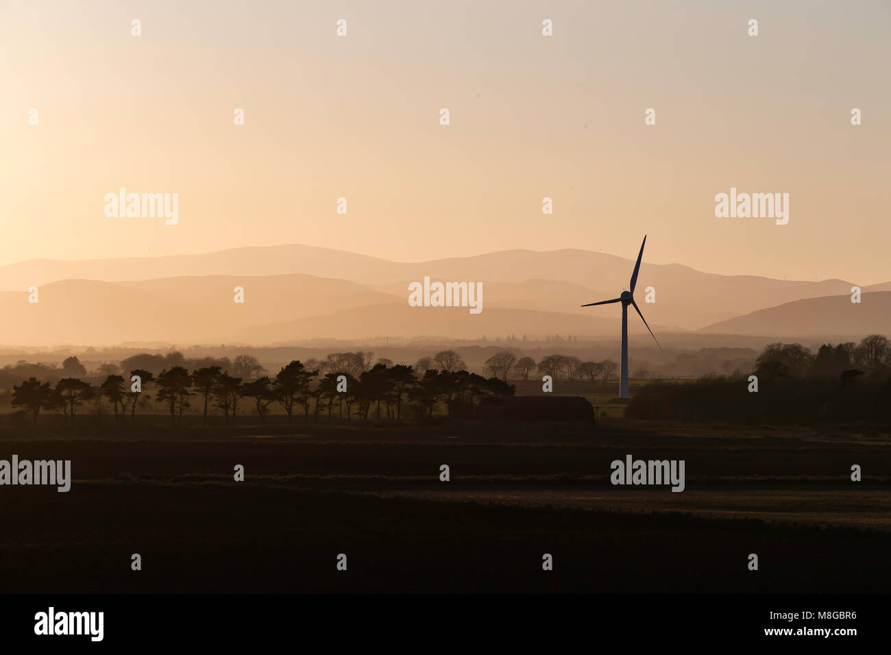 Single wind turbine in Easter Ross, Scotland in setting sun with recession landscape and hills in background. Stock Photo
