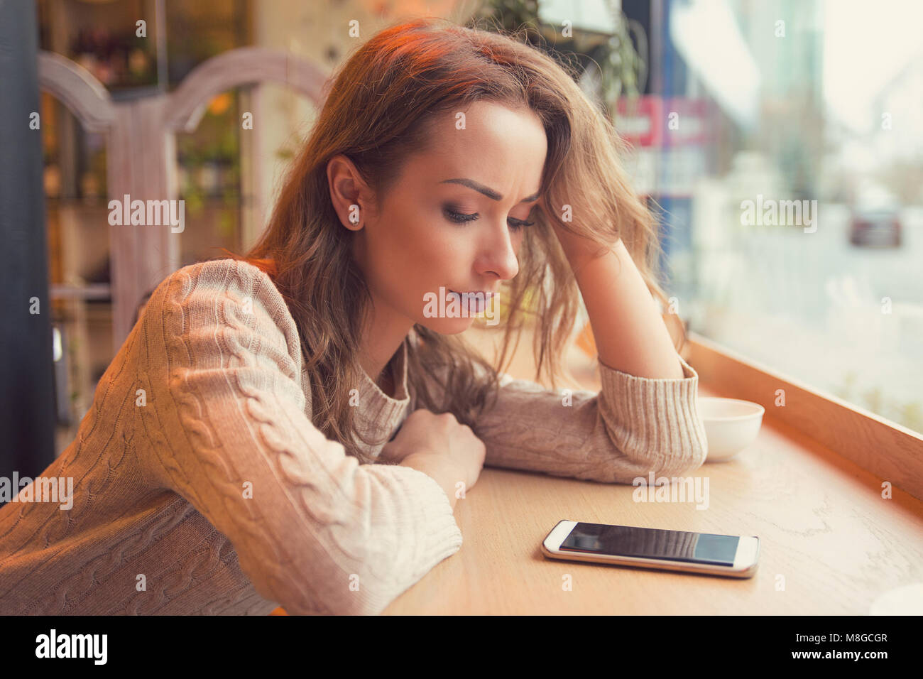 Young woman sitting at table in cafe looking at phone being