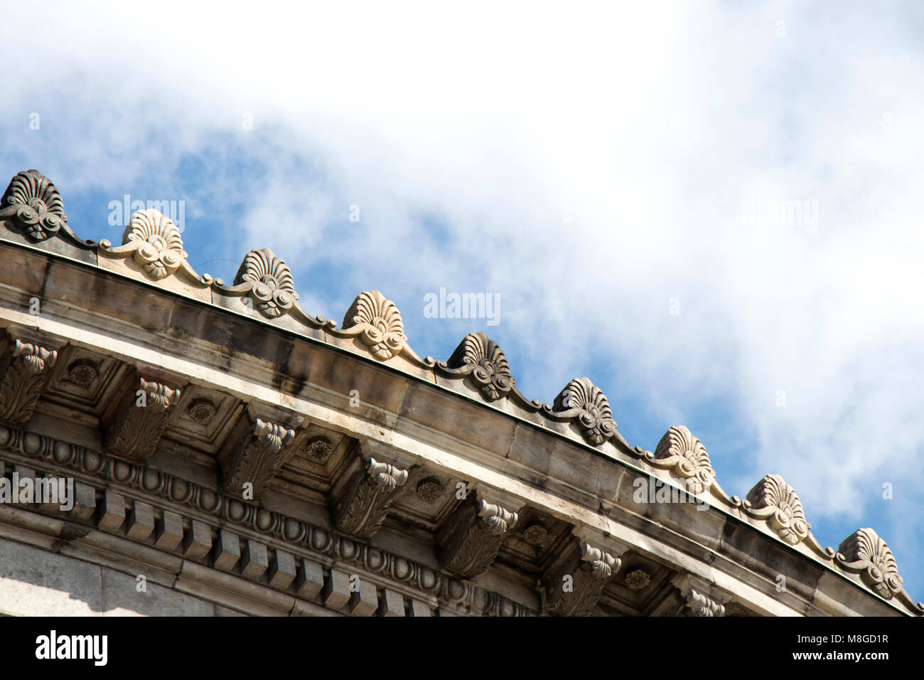 Detail of a neoclassical building with round cornice ornaments against a blue sky with white clouds Stock Photo