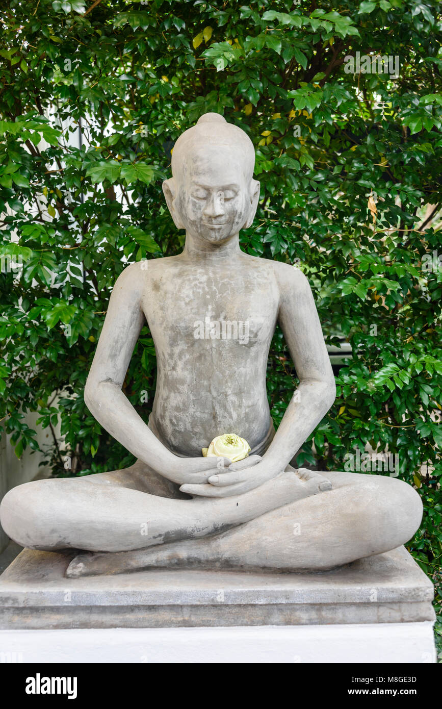 Stone statue of Buddha holding a lotus flower in a garden Stock Photo