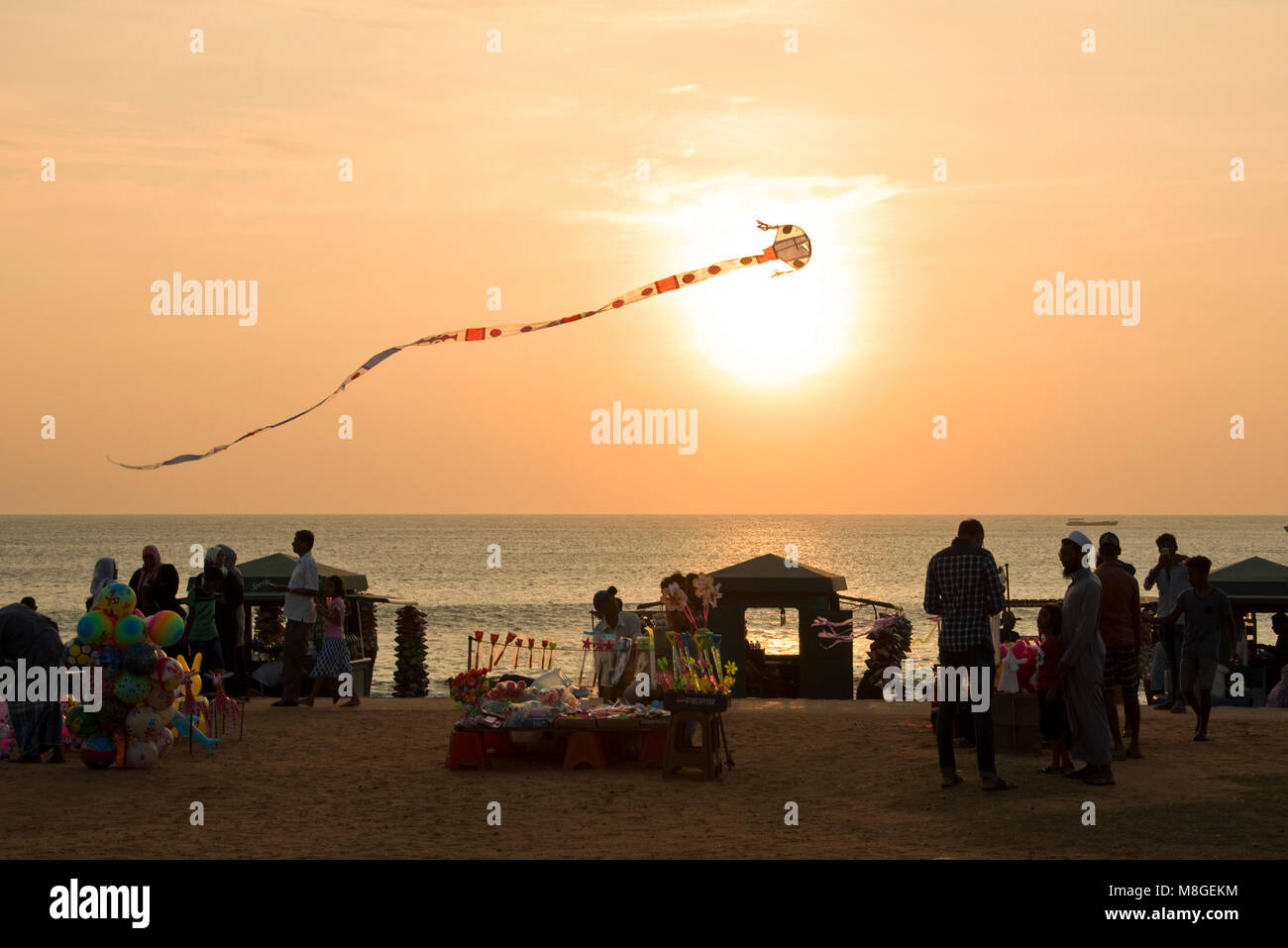 Local people and stall holders with a kite in the air on Galle Face Green at sunset - a popular spot in Colombo to spend time playing by the sea. Stock Photo
