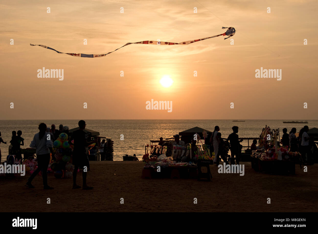 Local people and stall holders with a kite in the air on Galle Face Green at sunset - a popular spot in Colombo to spend time playing by the sea. Stock Photo