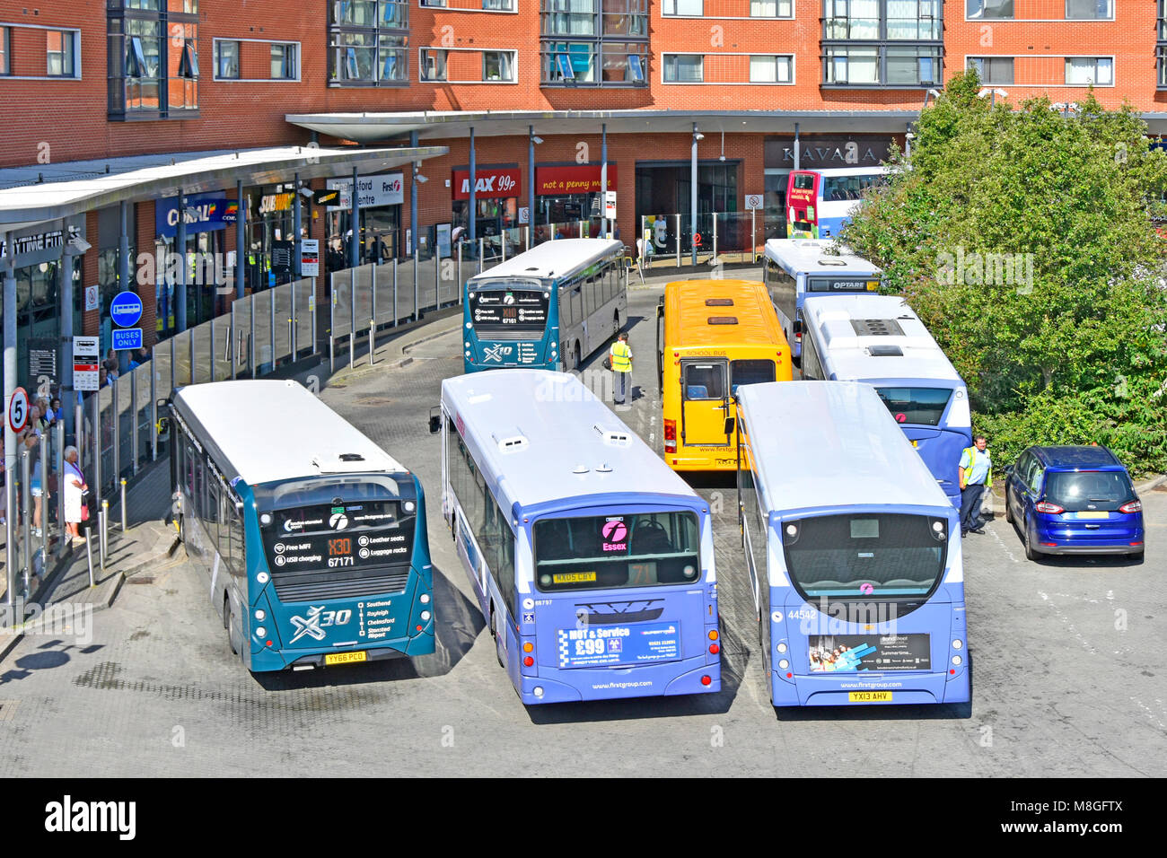 View from above looking down at buses Chelmsford town centre public transport bus station small selection retail shops behind passenger waiting area Stock Photo