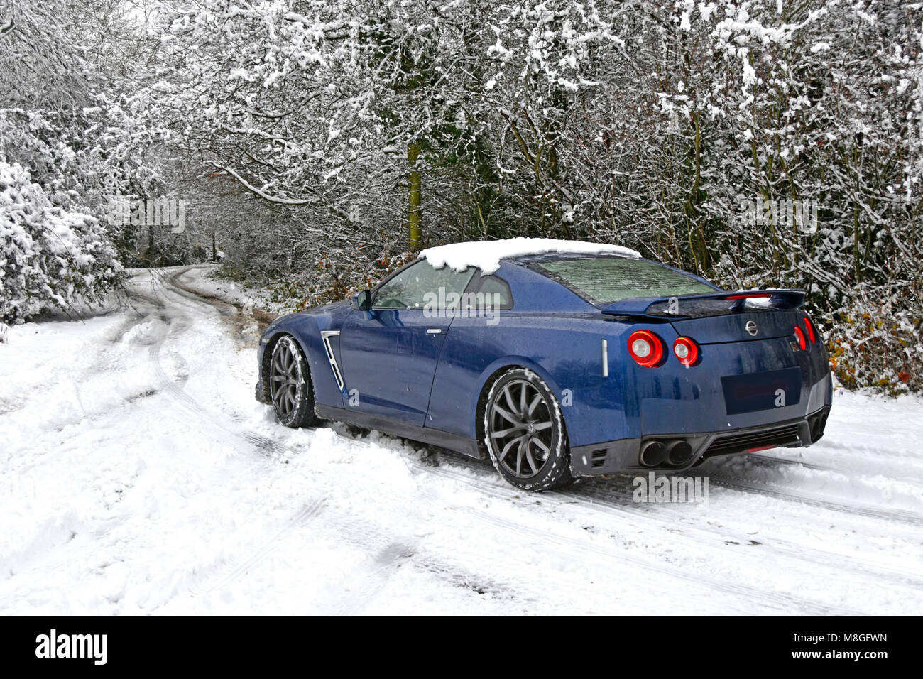 Poor weather for driving Nissan car along snow covered country lane in winter snow scene in snowy rural Brentwood Essex England UK Stock Photo