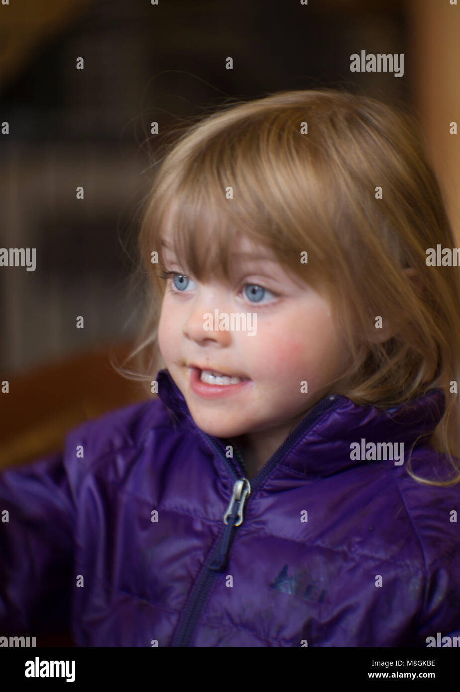 Candid portrait of a young girl with blond hair and blue eyes, wearing a purple jacket. Stock Photo