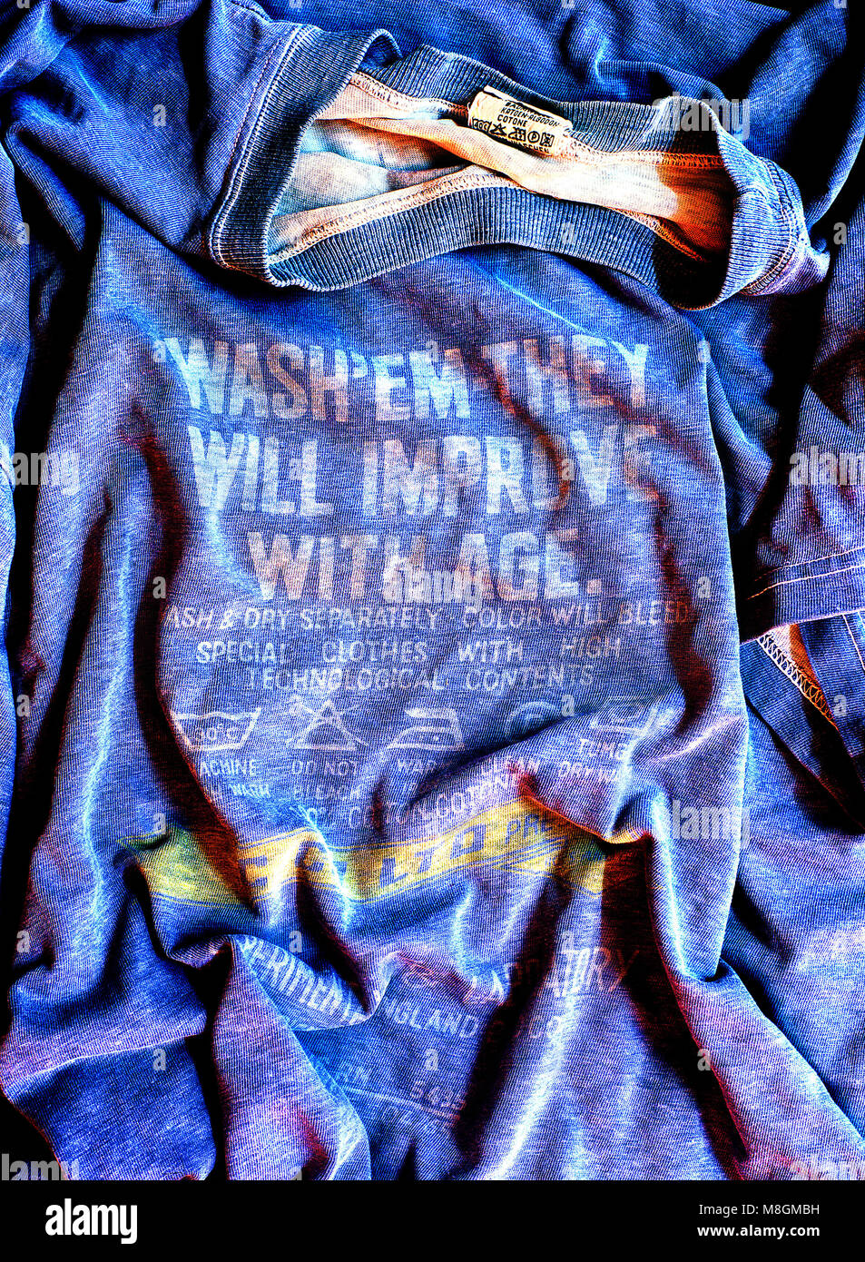 Blue wrinkled t-shirt with yellow faded text and symbols. Text reads: "Wash 'em they will improve with age. Stock Photo