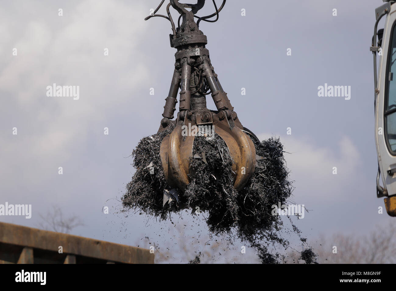 A worker uses a claw excavator to load shredded metal from cars at a