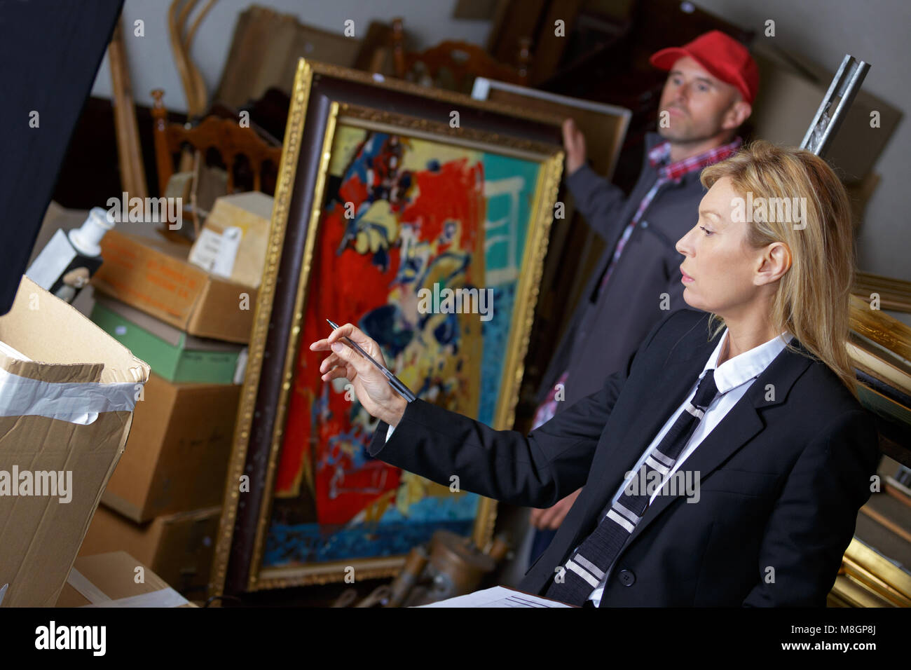female auctioneer showing her assistant which paintings to take Stock Photo