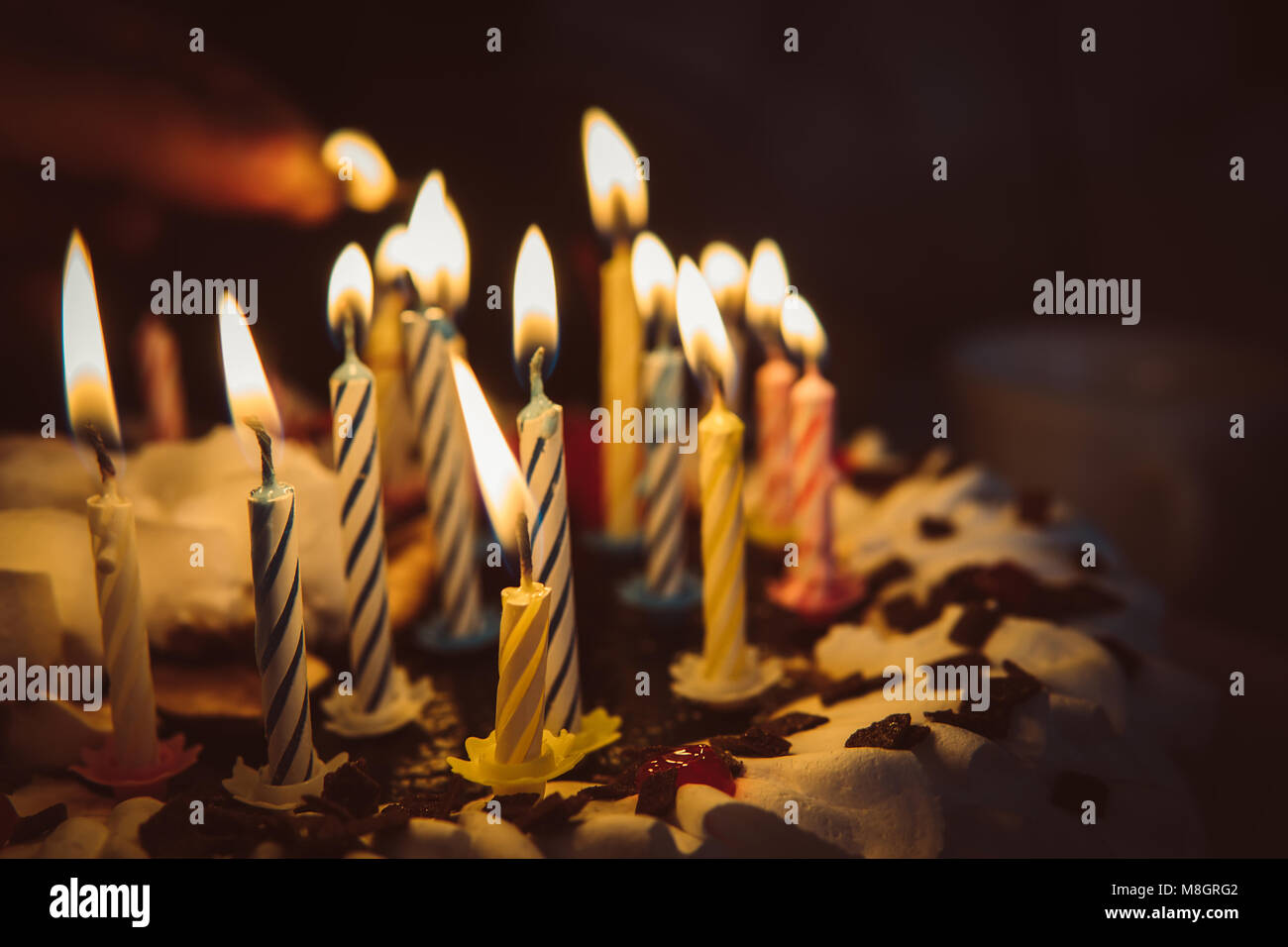 anniversary cake with hand burning candles in dark. A hand with a match  lights the candles on the birthday cake with white cream. 14 fourteen  candles Stock Photo - Alamy