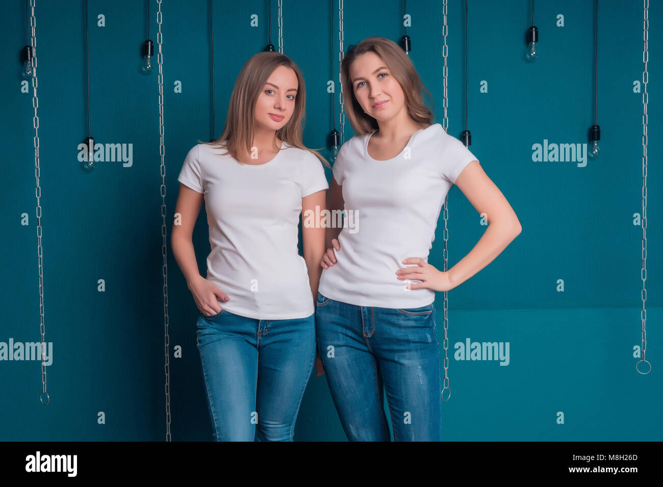 Portrait of girlfriends in white T-shirts and jeans on a dark background Stock Photo