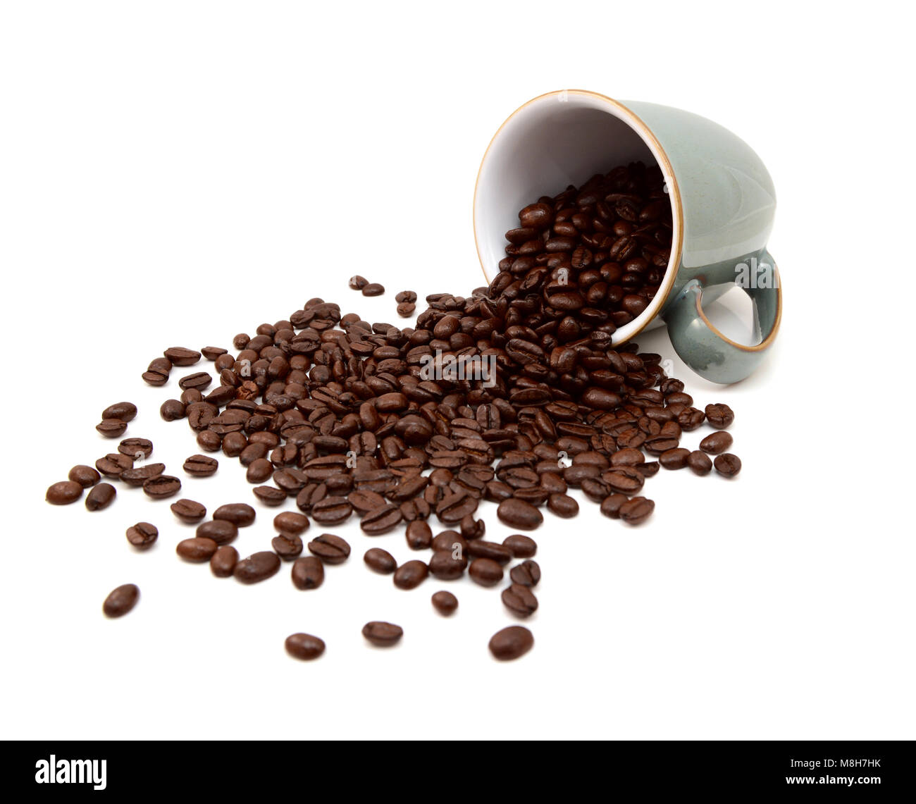 Aromatic roasted coffee beans pouring out from a green china mug on a