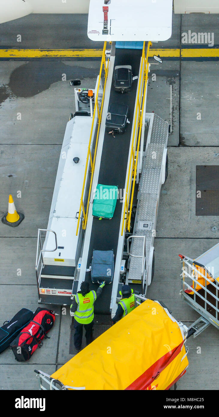London Gatwick, March 15th, 2018: High perspective of baggage handlers picking up suitcases from a conveyor belt connected to an Airbus A320 easyJet a Stock Photo